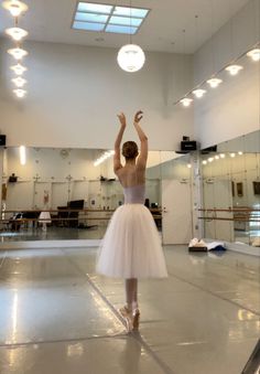 a ballerina in a white tutu is dancing with her arms up and head turned to the side