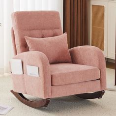 a pink rocking chair with pillows on it in front of a white wall and brown curtains