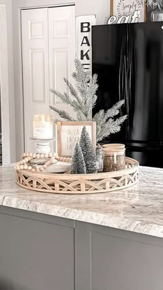 a kitchen counter topped with a tray filled with pine trees and candles next to a refrigerator