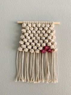 a wall hanging made out of yarn with beads and flowers on the front, along with two wooden pegs