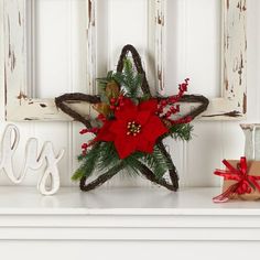 a star decoration with red poinsettia and greenery sits on a mantle