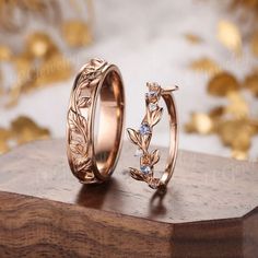 two gold rings with leaves on them sitting on top of a wooden table next to confetti