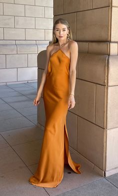 a woman in an orange dress leaning against a wall