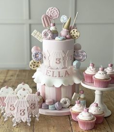 a pink and white birthday cake surrounded by cupcakes