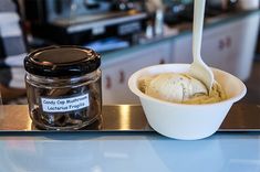 a bowl of ice cream next to a jar of cookies on a counter top with a spoon in it