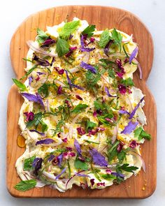 a wooden cutting board topped with salad on top of a white table next to a knife