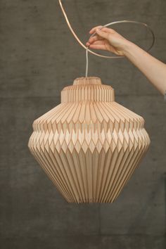 a hand holding a light fixture made out of wooden strips and plexed paper