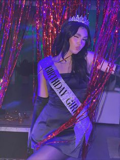 a woman wearing a tiara and posing in front of pink streamers with her hands on her hips