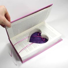 a hand is holding an open book with a purple heart inside it and string on the pages