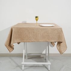 a table with a wine glass and plate on it in front of a white wall