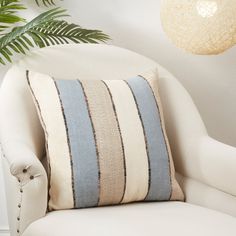 a white chair with a blue and beige striped pillow on it next to a potted plant