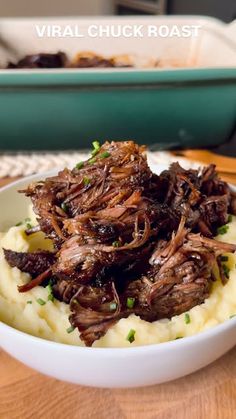 a white bowl filled with meat and mashed potatoes on top of a wooden table