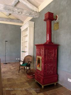 a red stove sitting in the corner of a room next to a chair and book shelf