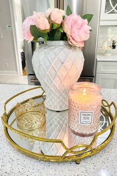 a white vase sitting on top of a table next to a candle and some pink flowers