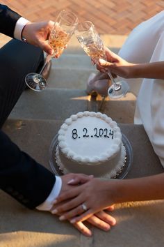 a newly married couple toasting champagne glasses over a cake on the steps outside their wedding reception