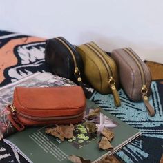 three small purses sitting on top of a bed next to an open book and some leaves