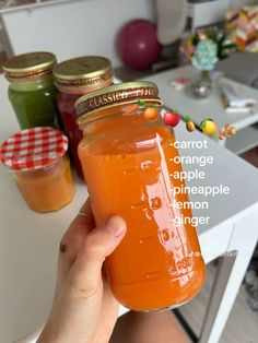 a person holding up a jar of carrot orange pineapple lemon ginger juice in front of some jars