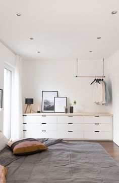 a bedroom with a bed, dresser and hanging clothes on the wall above it's headboard