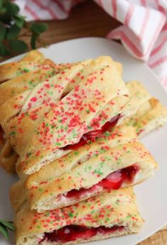 strawberry shortbreads with sprinkles on a white plate next to green leaves