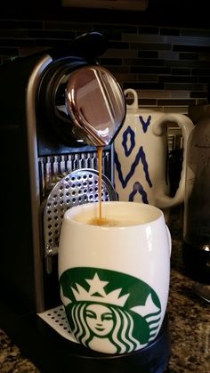 a starbucks coffee cup is being filled with liquid from a coffee maker on the counter