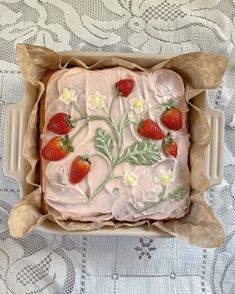 a cake with frosting and strawberries in a box on a tableclothed surface