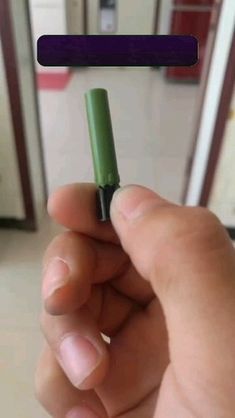 a hand holding a small green object in front of the camera with an eraser on it