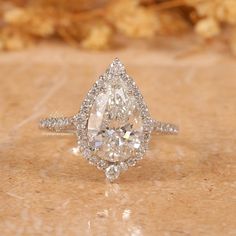 a pear shaped diamond engagement ring on a marble surface with gold flowers in the background