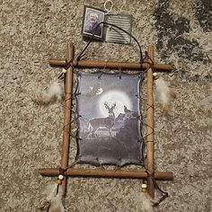 a wooden frame with some pictures and feathers hanging from it's sides on the floor