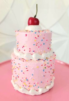 a three layer pink cake with sprinkles and a cherry on the top