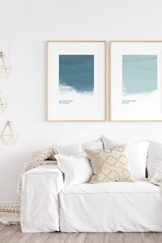 two framed pictures hang on the wall above a white couch in a room with wood flooring