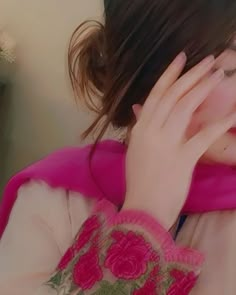 a woman wearing a pink scarf covering her face and holding her hand to her eye