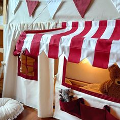 a teddy bear is sitting in a tent with red and white stripes on the walls