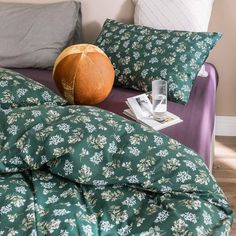 a bed with green and white floral comforter next to a purple couch in a bedroom