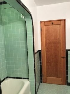 a green tiled bathroom with a wooden door and bathtub in the corner next to it