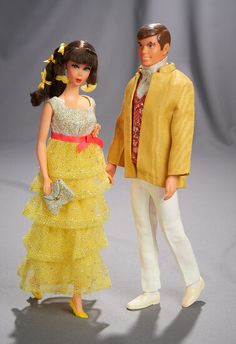 a barbie doll is standing next to a man in a yellow suit