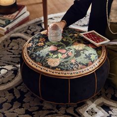 a woman sitting on top of a black ottoman next to a table with a book