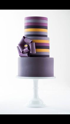 a three tiered cake with purple, yellow and pink ribbons on it's side