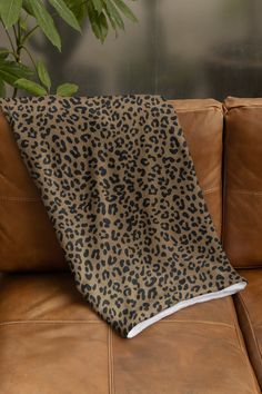 a leopard print blanket sitting on top of a brown couch next to a potted plant