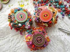 three colorful brooches sitting on top of a white lace covered table next to scissors