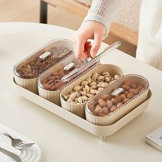 a person picking nuts from three containers on a table next to a cell phone and silverware