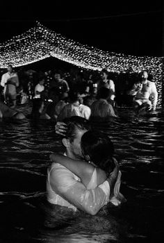 black and white photograph of people in water at night with lights on the wall behind them