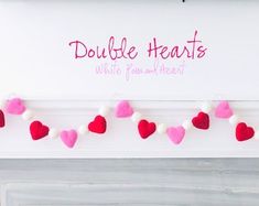 red and pink felt hearts are hanging on a white wall with the words double hearts written above them