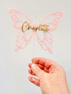 a hand holding a pink butterfly shaped cake topper with the word charlotte on it