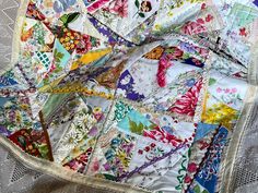 an old quilt is laying on top of a lace tablecloth with colorful flowers and leaves