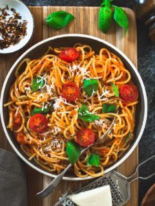 a bowl of spaghetti with tomatoes and parmesan cheese on a wooden cutting board