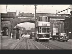 an old black and white photo of a double decker bus on the street in front of a bridge