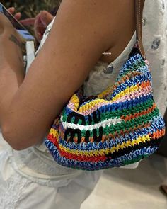 a woman is holding a crocheted purse and looking at her cell phone