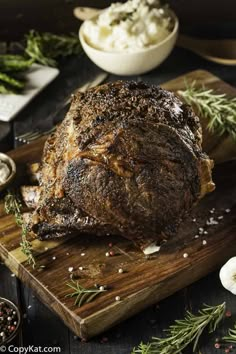 a large piece of meat sitting on top of a wooden cutting board next to garlic and seasoning