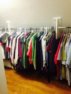 a room filled with lots of different colored shirts hanging on clothes racks and wooden floors