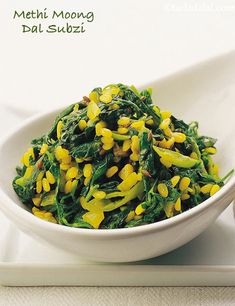 a white bowl filled with green and yellow food on top of a table next to a spoon